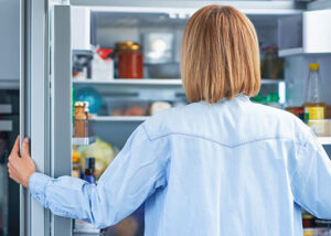 dame, die nach dem essen mit hungerschmerzen in den kühlschrank schaut