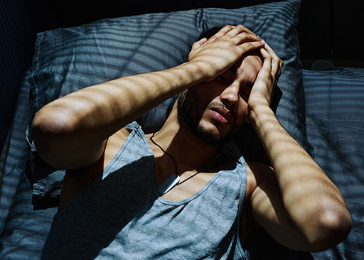 weißer Mann, der im Bett liegt und aufgrund von Entzugskopfschmerzen nicht schlafen kann
